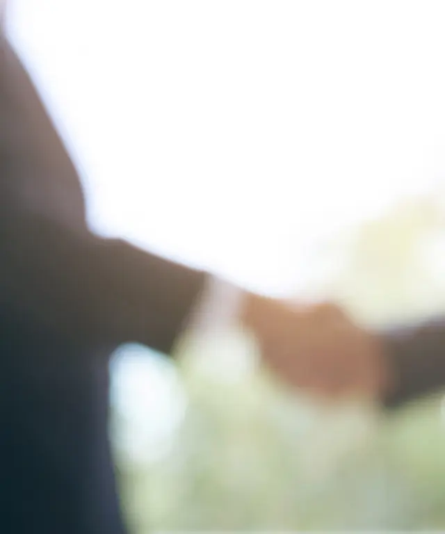 Zwei Geschäftsleute geben sich vor unscharfem Hintergrund die Hand – Symbol für Kooperation, Vertrauen und erfolgreiche Zusammenarbeit.