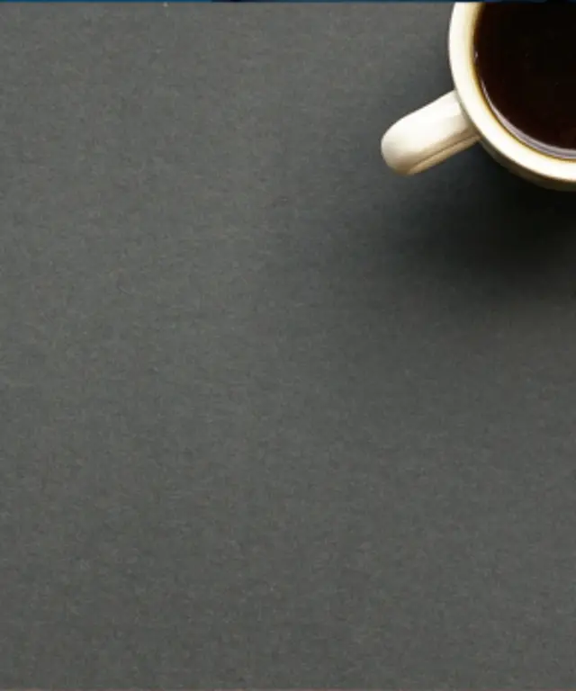 Minimalistischer Arbeitsplatz mit Laptop und Kaffee auf dunkler Oberfläche – moderner, aufgeräumter Office‑Look mit viel Freifläche.