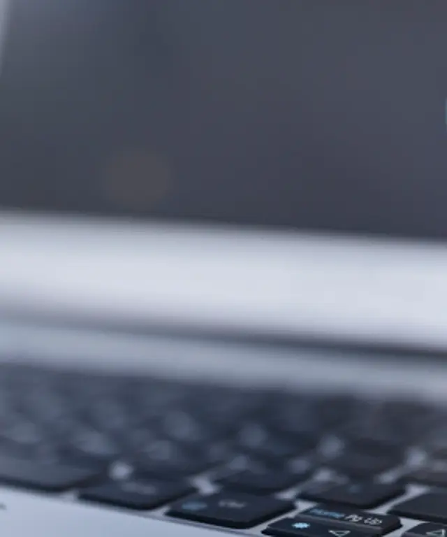 Kleines Stundenglas mit blauem Sand auf einer Laptop‑Tastatur – Symbol für Zeitmanagement, Deadline‑Druck und digitale Arbeitsprozesse.