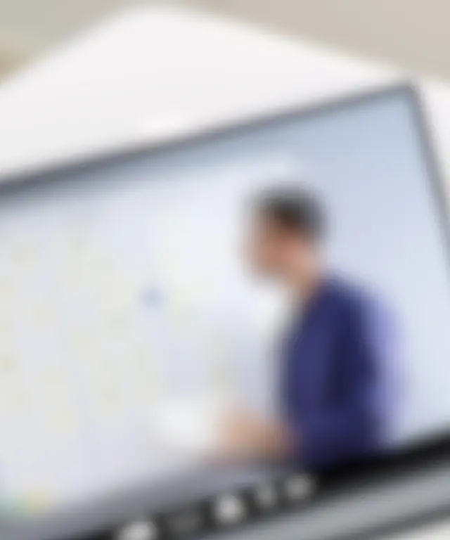 Person verfolgt eine Online‑Schulung auf einem Tablet, während ein Dozent an einem digitalen Whiteboard erklärt – modernes E‑Learning‑Szenario.