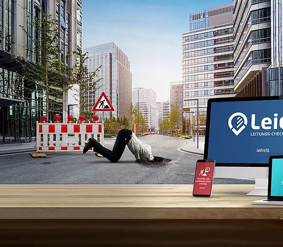 Holztisch mit Monitor, Tablet und Smartphone, die Leico‑Oberflächen zeigen. Dahinter eine städtische Straße mit Baustellenabsperrung und einer Person, die in ein Loch gestürzt ist.