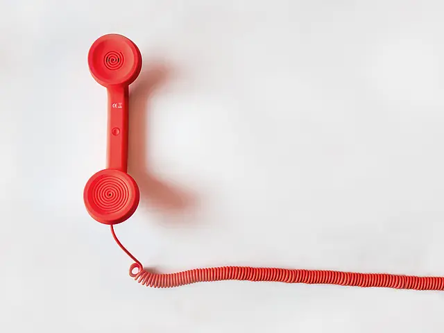 Roter Telefonhörer mit Spiralkabel auf hellem Hintergrund Roter, klassischer Telefonhörer liegt mit langem Spiralkabel auf einer hellen Fläche; minimalistische, klare Draufsicht.