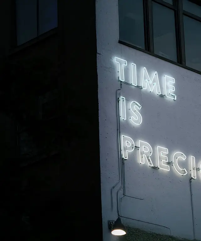 Neon-Schriftzug ‚Time is Precious‘ leuchtet an einer dunklen Hausfassade bei Nacht – urbanes Street‑Setting mit Fenstern und Lampe